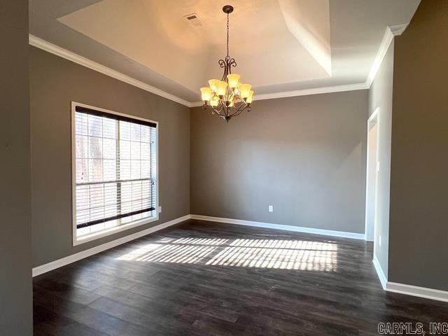 spare room featuring an inviting chandelier, dark hardwood / wood-style flooring, ornamental molding, and a tray ceiling