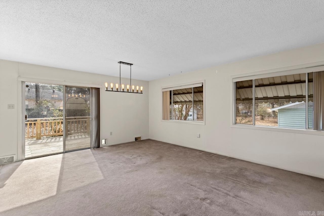 spare room featuring a textured ceiling, carpet flooring, a chandelier, and a healthy amount of sunlight