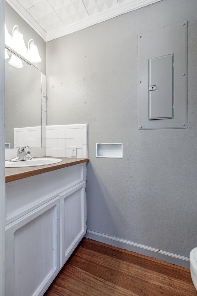 bathroom featuring electric panel, hardwood / wood-style flooring, decorative backsplash, ornamental molding, and vanity