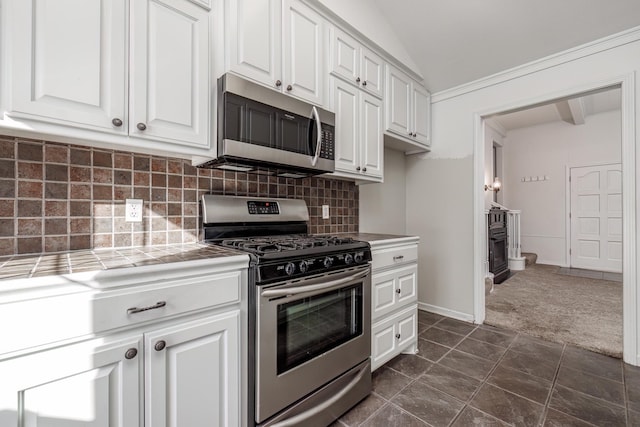 kitchen with dark colored carpet, stainless steel appliances, tile counters, vaulted ceiling, and white cabinets