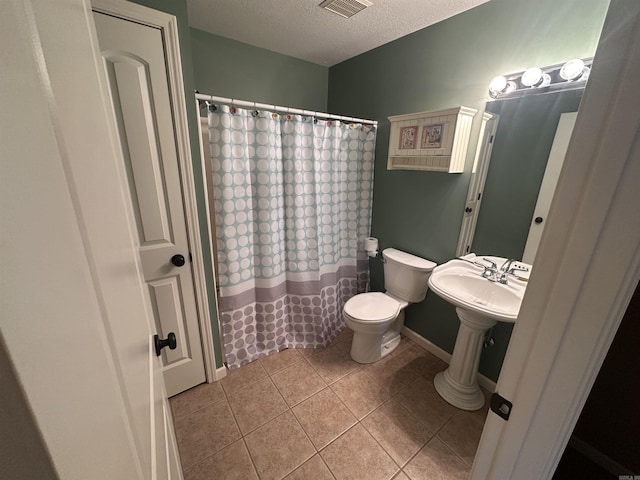 bathroom featuring toilet, curtained shower, tile patterned flooring, and a textured ceiling