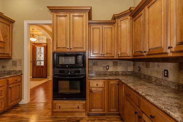 kitchen featuring wood-type flooring, light stone countertops, backsplash, and black appliances