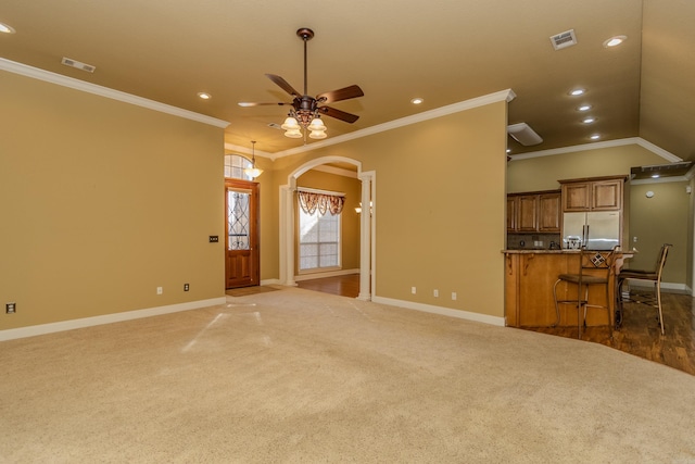 unfurnished living room with ornamental molding, ceiling fan, and dark colored carpet