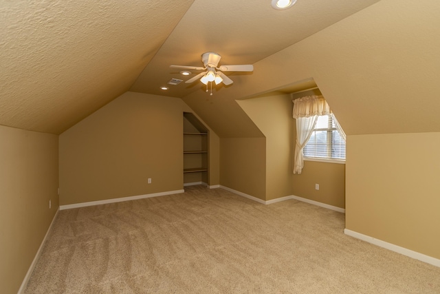 bonus room with ceiling fan, vaulted ceiling, light colored carpet, and a textured ceiling