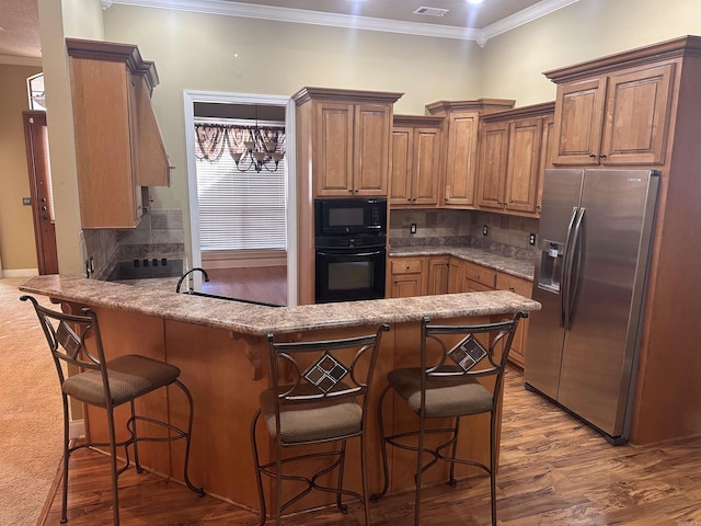 kitchen featuring hardwood / wood-style flooring, a breakfast bar area, tasteful backsplash, black appliances, and kitchen peninsula