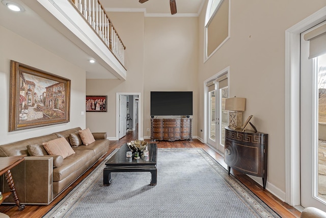 living room featuring ceiling fan, a high ceiling, ornamental molding, and hardwood / wood-style flooring