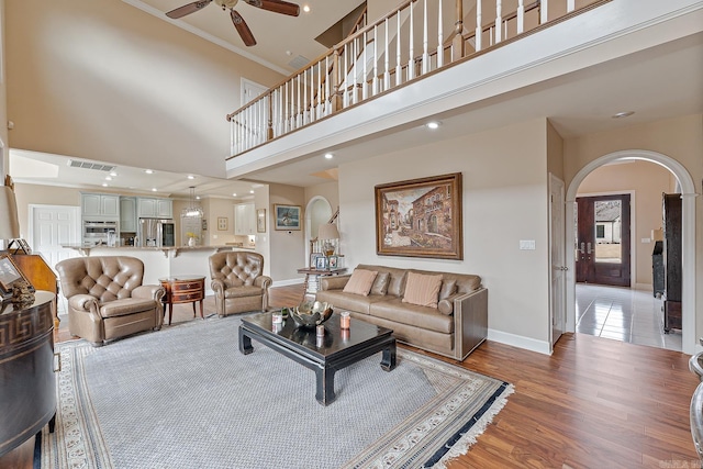 living room with ceiling fan, a high ceiling, and light hardwood / wood-style flooring