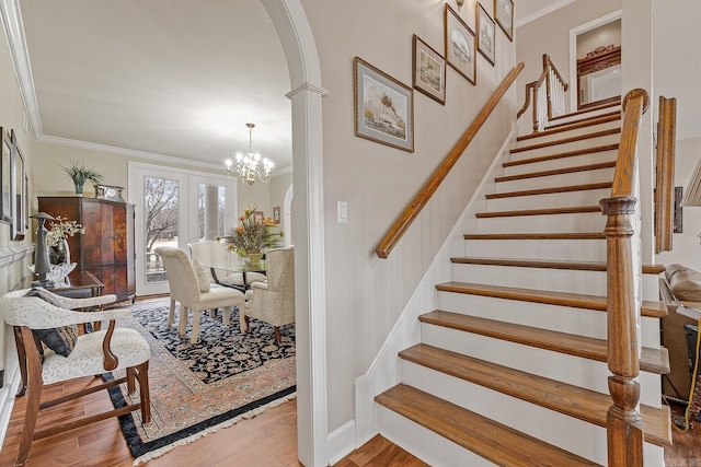 staircase featuring wood-type flooring, crown molding, and a chandelier