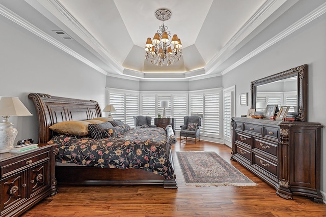 bedroom with wood-type flooring, crown molding, a raised ceiling, and an inviting chandelier