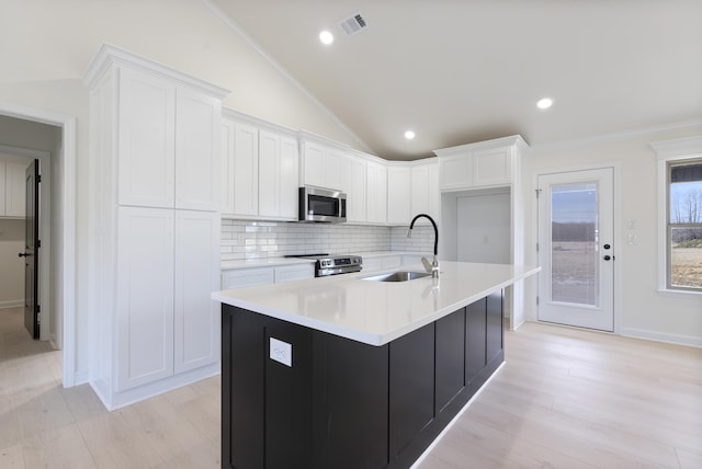 kitchen with white cabinets, appliances with stainless steel finishes, lofted ceiling, sink, and a center island with sink