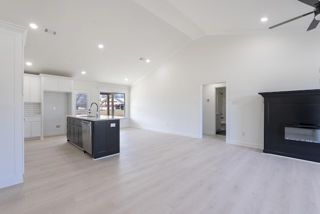 kitchen featuring vaulted ceiling, a center island with sink, stainless steel dishwasher, sink, and white cabinetry