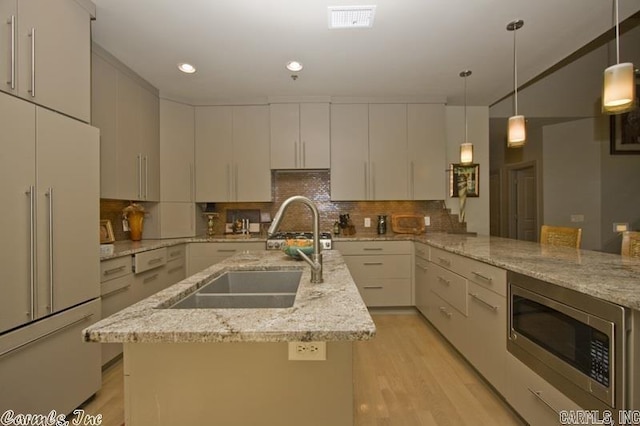 kitchen with pendant lighting, decorative backsplash, sink, built in appliances, and light stone countertops