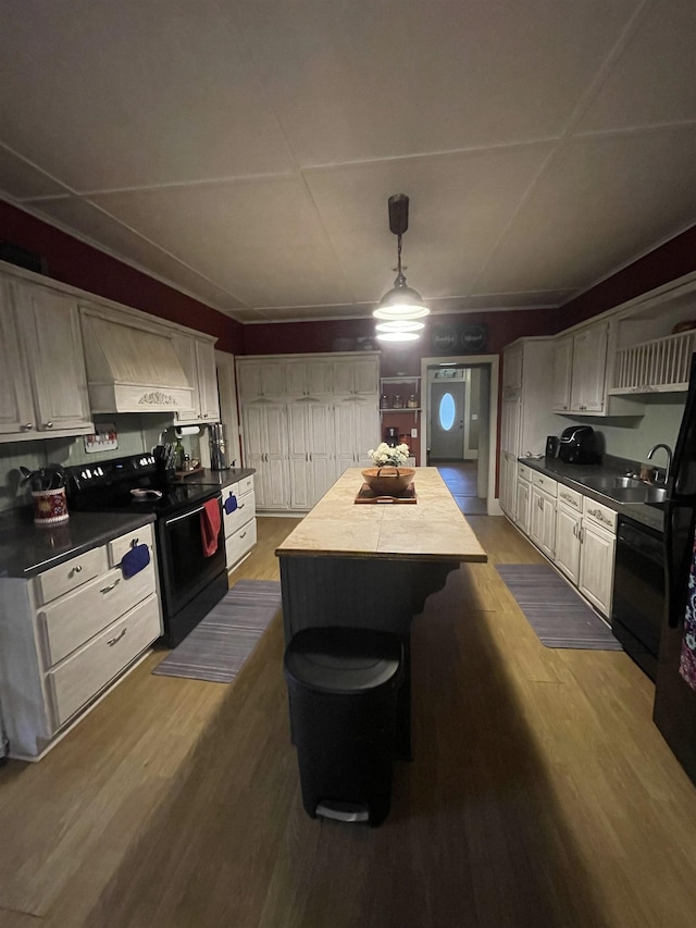 kitchen featuring pendant lighting, hardwood / wood-style floors, black appliances, a kitchen island, and custom range hood