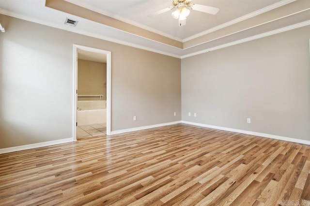 empty room with ceiling fan, light wood-type flooring, a tray ceiling, and ornamental molding