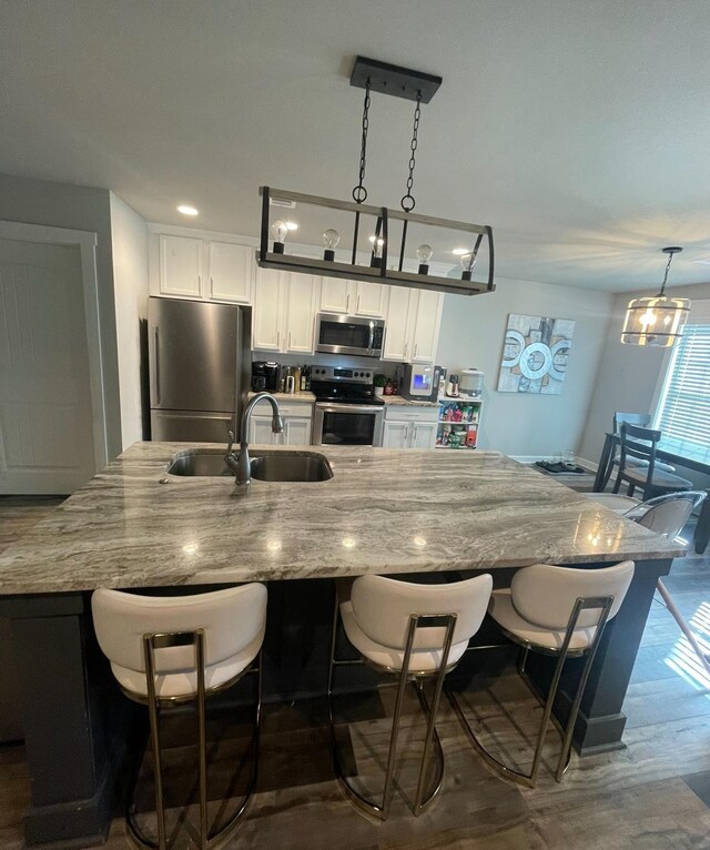 kitchen featuring sink, appliances with stainless steel finishes, hanging light fixtures, a kitchen breakfast bar, and white cabinets