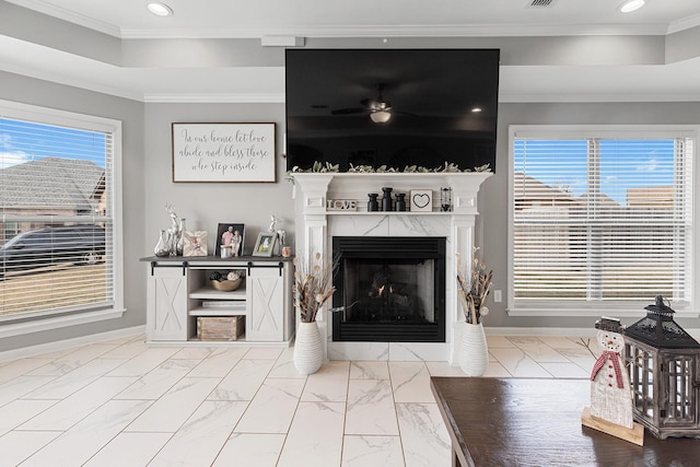 living room with ceiling fan, ornamental molding, a premium fireplace, and a healthy amount of sunlight