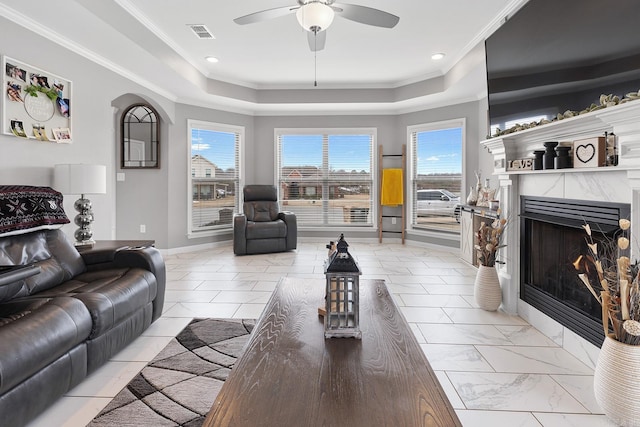 living room featuring a premium fireplace, crown molding, a raised ceiling, and ceiling fan