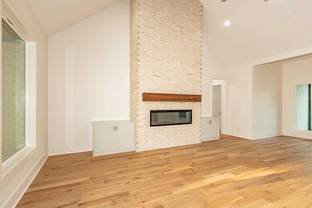 unfurnished living room with light hardwood / wood-style floors, a stone fireplace, and high vaulted ceiling