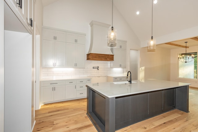 kitchen featuring white cabinets, tasteful backsplash, sink, a center island with sink, and custom range hood