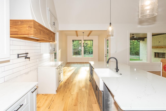 kitchen featuring white cabinets, decorative light fixtures, sink, backsplash, and light stone counters