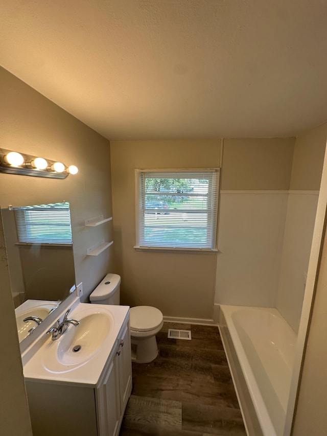 bathroom featuring toilet, vanity, a tub, and hardwood / wood-style floors