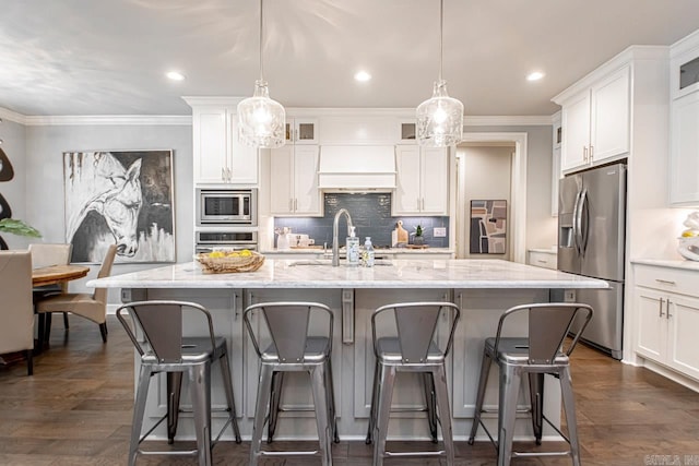 kitchen featuring pendant lighting, appliances with stainless steel finishes, white cabinetry, an island with sink, and sink