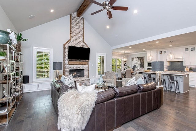 living room with dark hardwood / wood-style flooring, ceiling fan, high vaulted ceiling, a brick fireplace, and beam ceiling