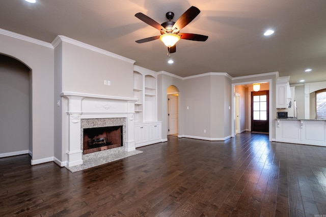 unfurnished living room featuring crown molding, ceiling fan, dark hardwood / wood-style flooring, built in features, and a tiled fireplace