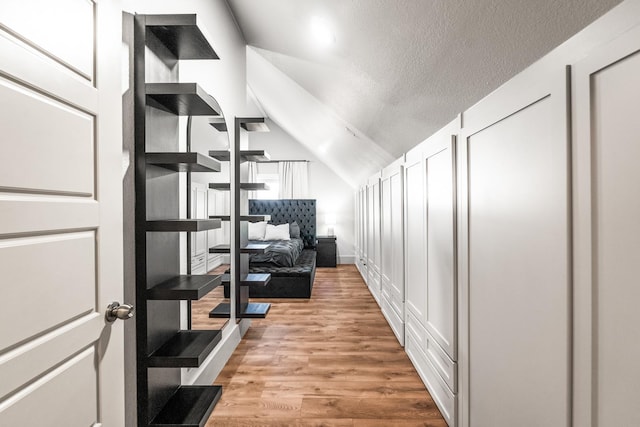 hall with a textured ceiling, lofted ceiling, and light wood-type flooring