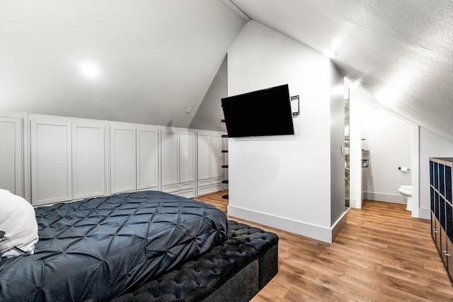 bedroom with vaulted ceiling, light hardwood / wood-style flooring, and ensuite bath