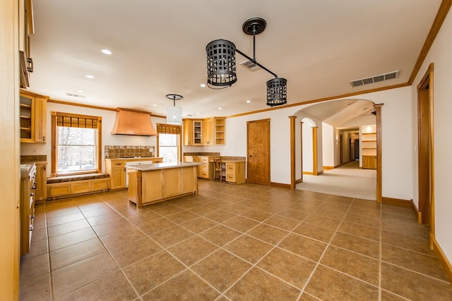 kitchen with a center island, tile patterned floors, premium range hood, hanging light fixtures, and crown molding