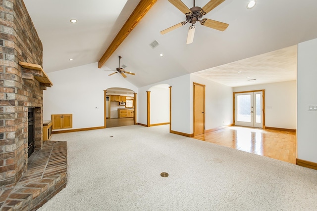 unfurnished living room with a fireplace, carpet floors, french doors, ceiling fan, and lofted ceiling with beams