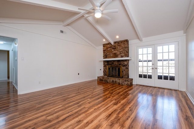 unfurnished living room with a stone fireplace, hardwood / wood-style flooring, french doors, ceiling fan, and lofted ceiling with beams