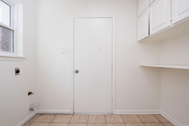 clothes washing area with hookup for an electric dryer, cabinets, and light tile patterned flooring