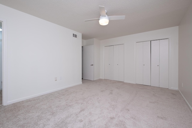 unfurnished bedroom with light carpet, ceiling fan, a textured ceiling, and two closets