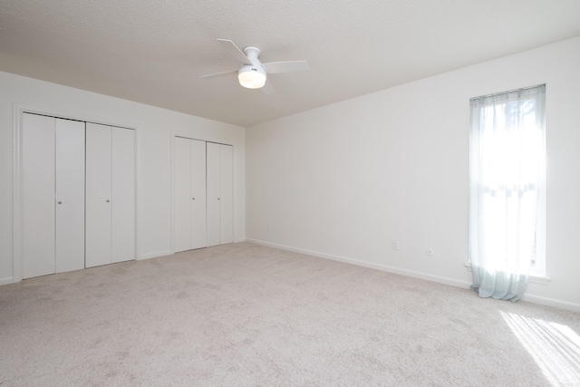 unfurnished bedroom featuring ceiling fan, light colored carpet, and two closets