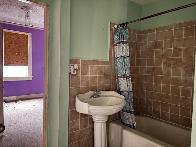 full bath with a wainscoted wall, a textured ceiling, shower / bath combo with shower curtain, and tile walls