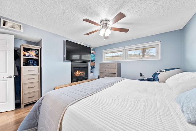 bedroom with ceiling fan, a textured ceiling, and light hardwood / wood-style flooring