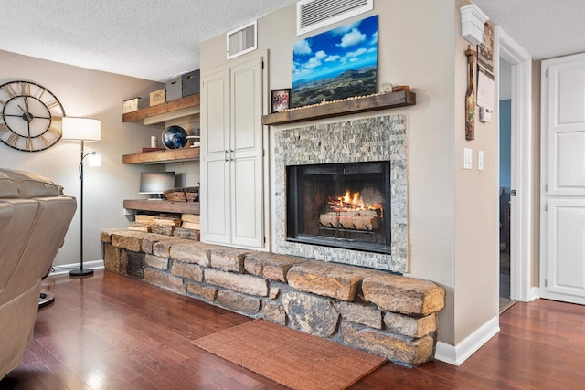 living room with a textured ceiling, a stone fireplace, and dark hardwood / wood-style flooring