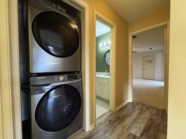 washroom with sink, wood-type flooring, stacked washer and clothes dryer, and a textured ceiling