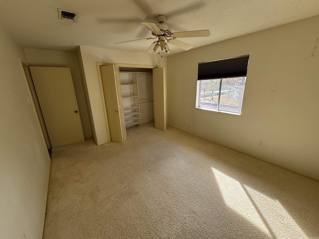 unfurnished bedroom with light carpet, a textured ceiling, a closet, and ceiling fan