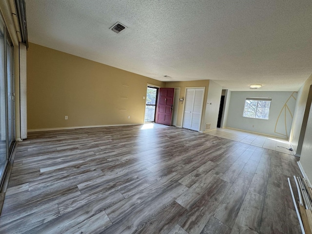 unfurnished living room with wood-type flooring, a textured ceiling, and a healthy amount of sunlight