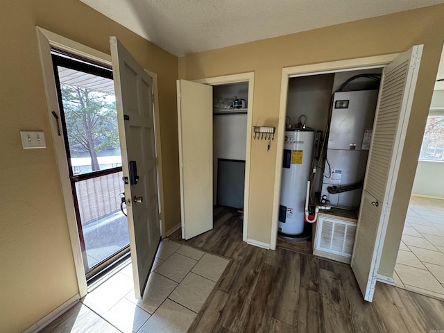 interior space with a textured ceiling, hardwood / wood-style floors, water heater, and heating unit