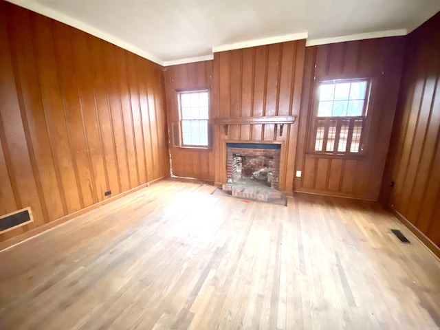 unfurnished living room featuring a brick fireplace, light hardwood / wood-style flooring, and wooden walls