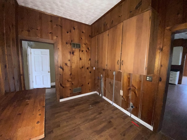 interior space with dark wood-type flooring, a textured ceiling, and wooden walls