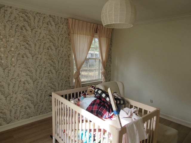 bedroom with hardwood / wood-style flooring, ornamental molding, and a crib