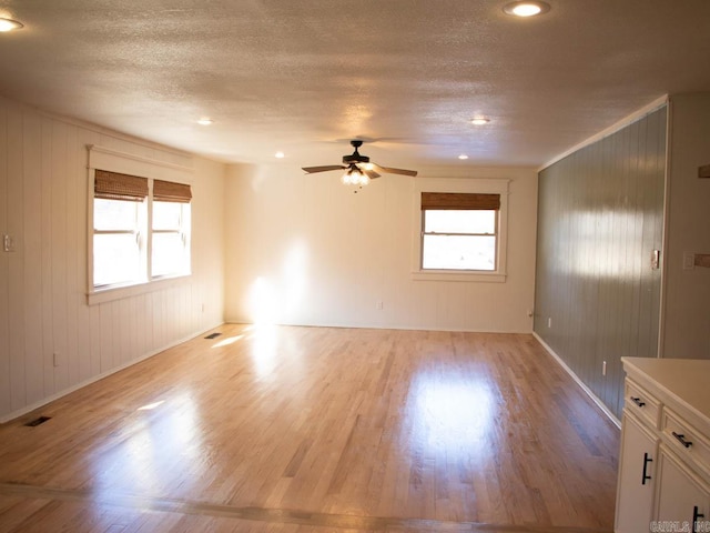 empty room with ceiling fan, light hardwood / wood-style flooring, wooden walls, and a textured ceiling