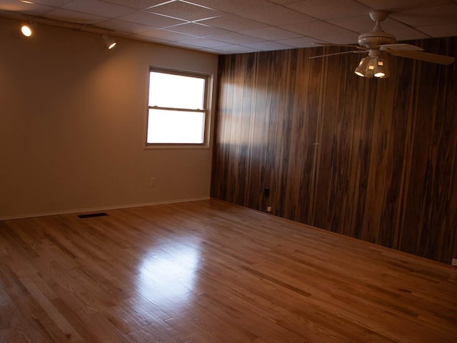 empty room featuring hardwood / wood-style floors, wooden walls, and ceiling fan