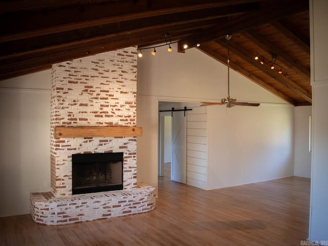 unfurnished living room featuring wood ceiling, a fireplace, lofted ceiling with beams, hardwood / wood-style flooring, and a barn door