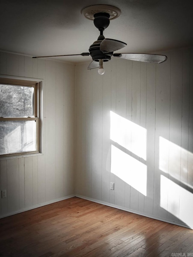 unfurnished room featuring light hardwood / wood-style floors, wood walls, and ceiling fan